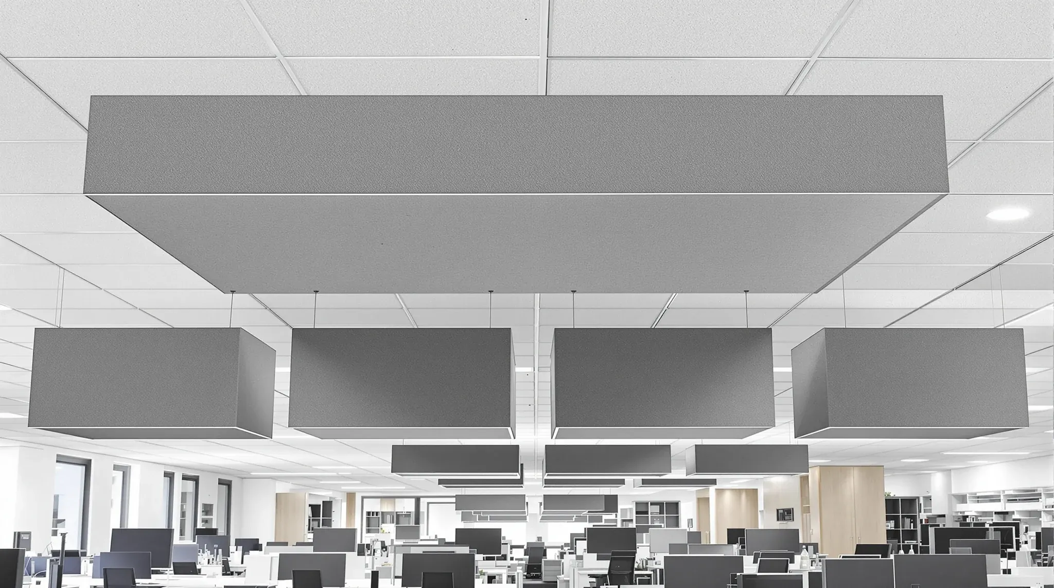 Four charcoal felt acoustic rafts hung on wires below a tiled office ceiling over a cluster of desks