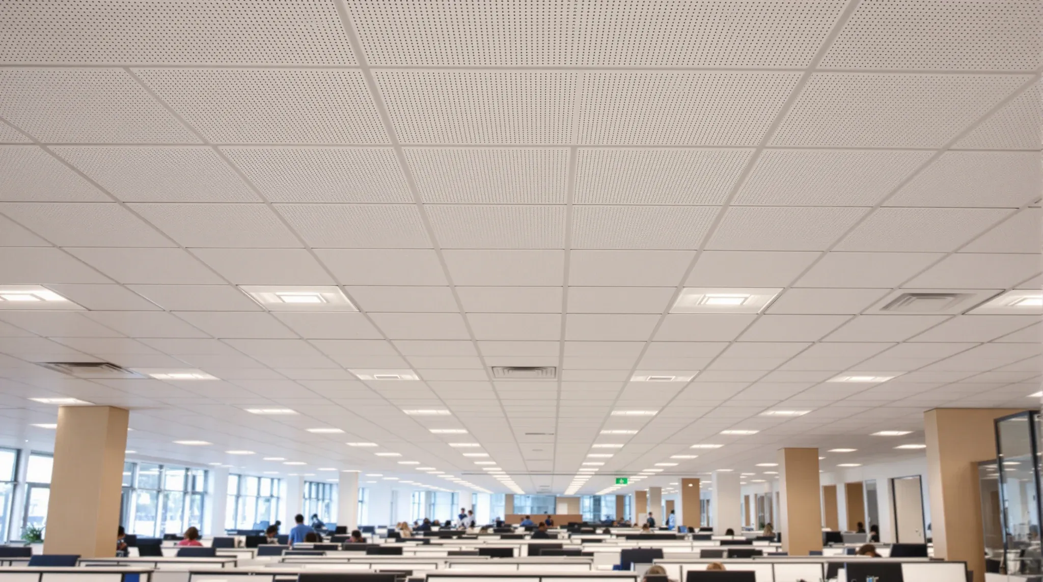 An open-plan office seen from a desk, with a wide matt acoustic tile ceiling above