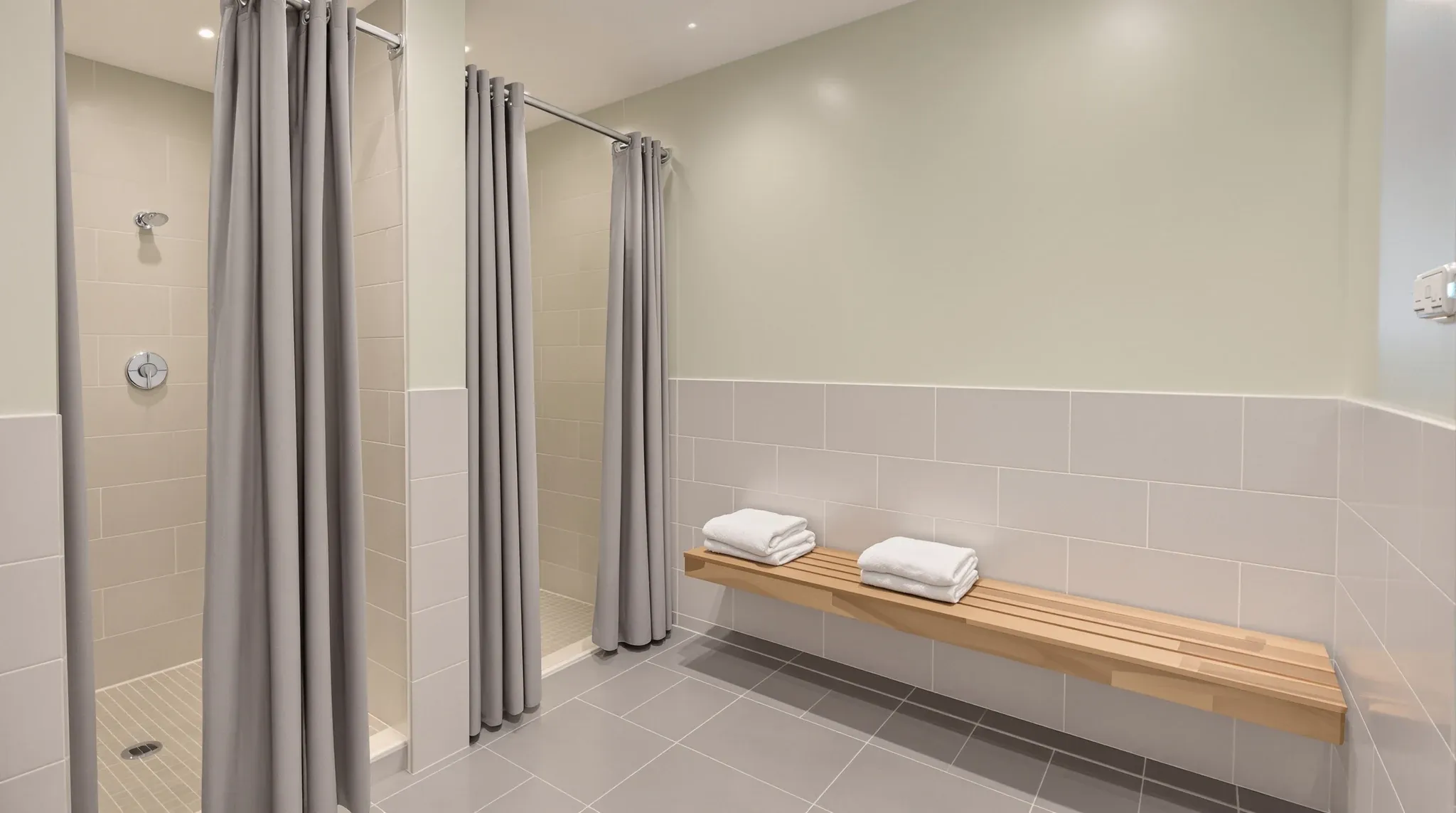 A basement end-of-trip change room with tiled shower bays, sage painted walls and a slatted timber bench