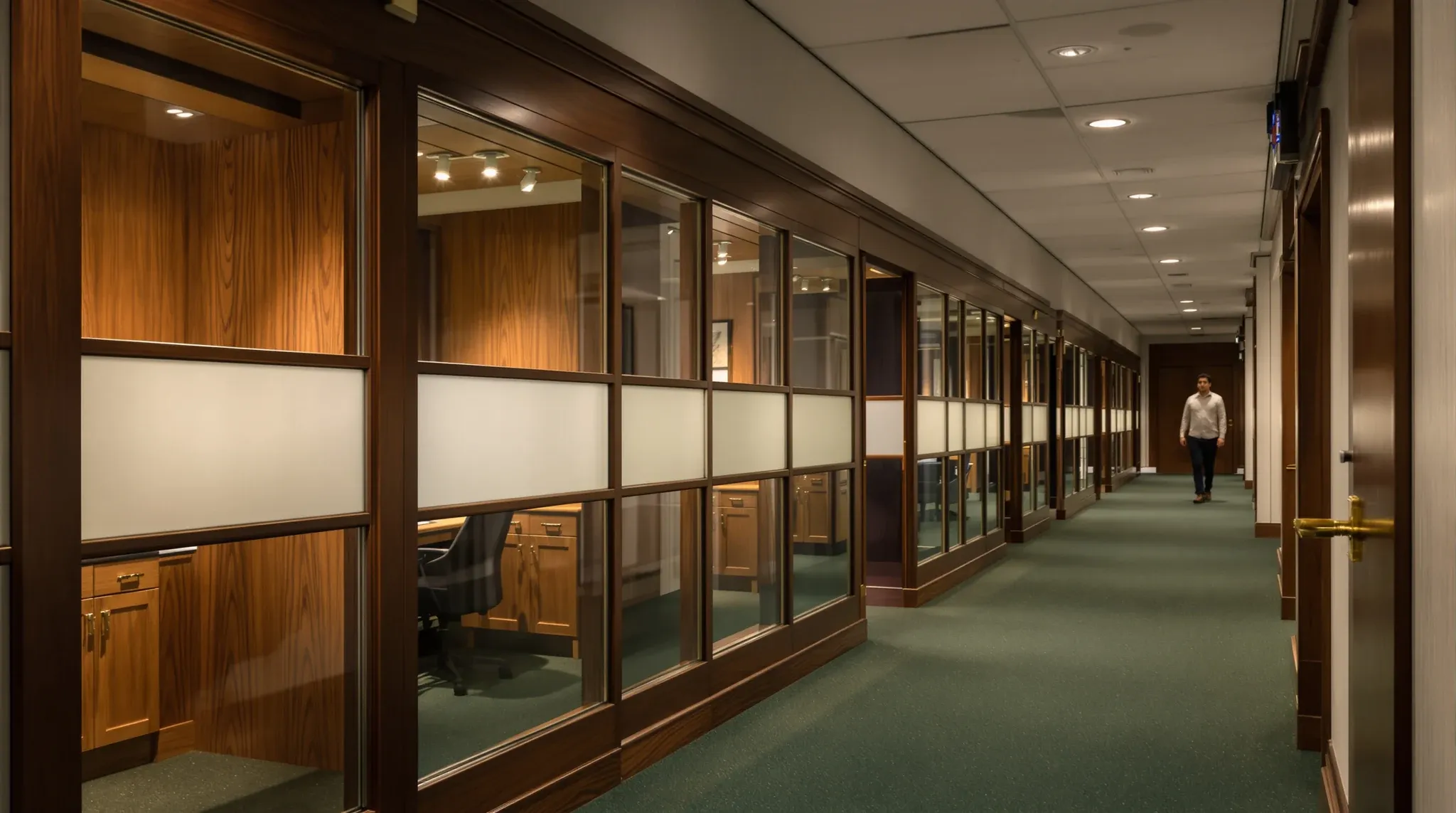 A quiet corridor of timber-framed glass private offices with frosted bands in a professional office