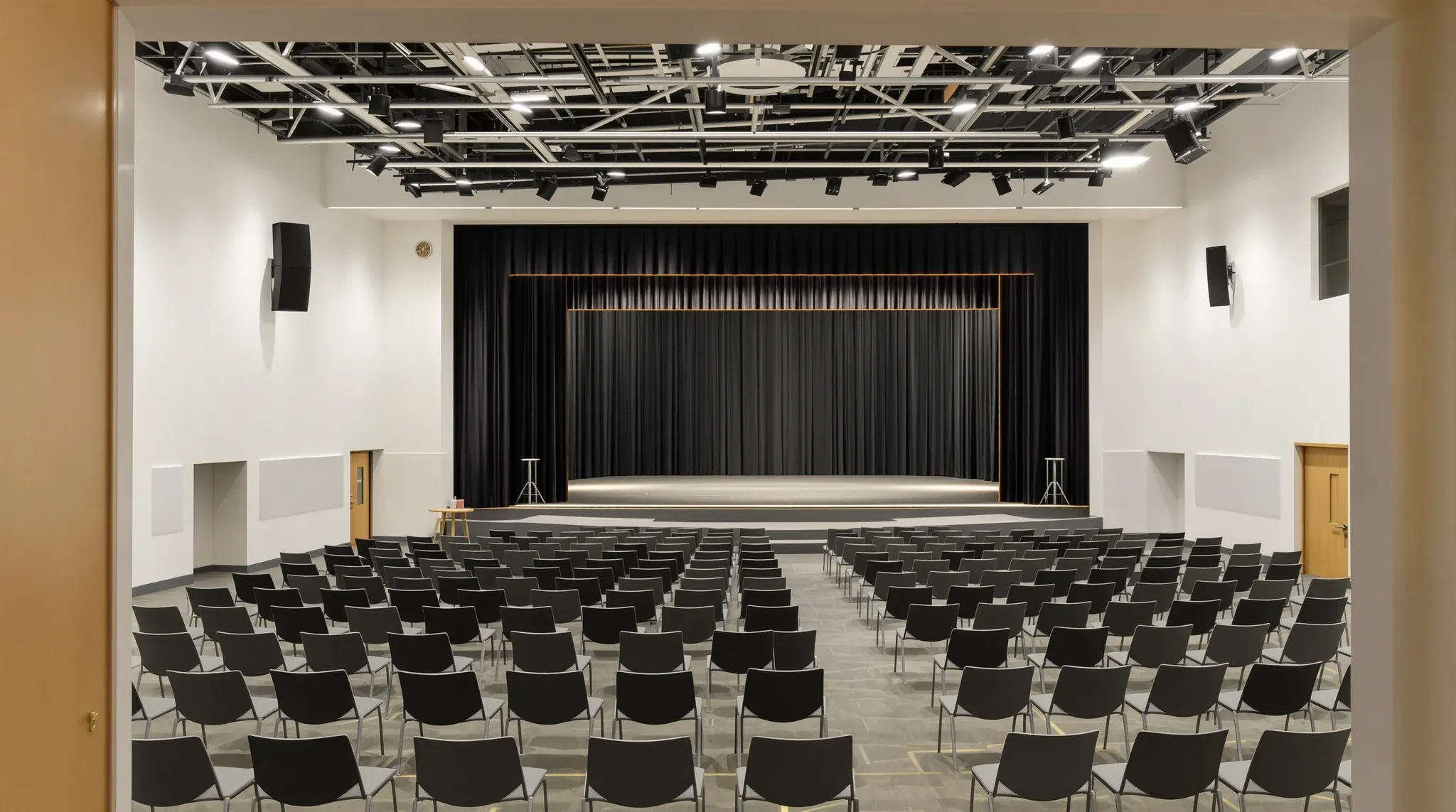 Empty finished hall with rows of chairs, stage with black backdrop, acoustic ceiling, no religious symbols or text
