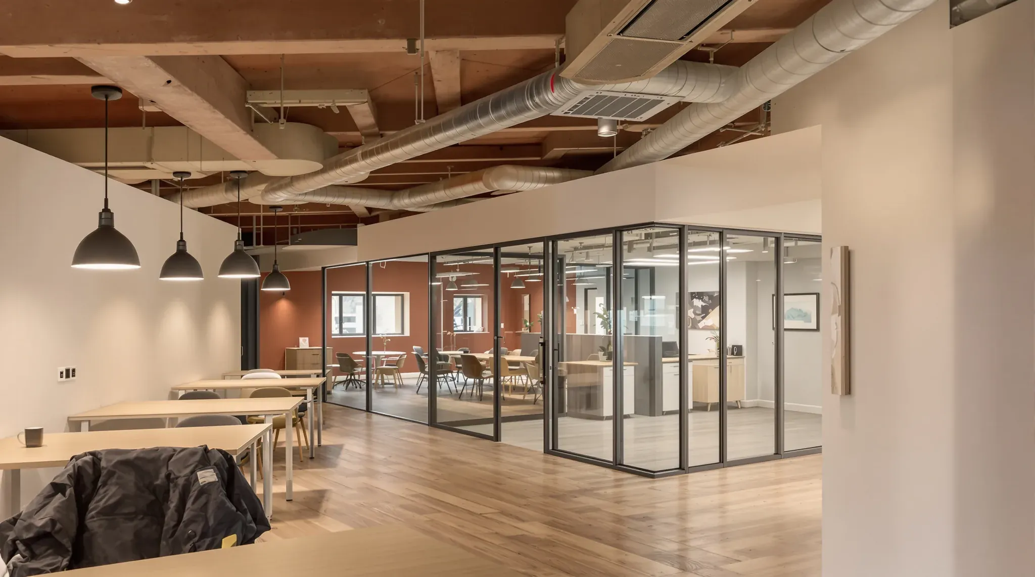 Basement office with a painted open ceiling and ducts, pendant lights over desks and glass-fronted rooms