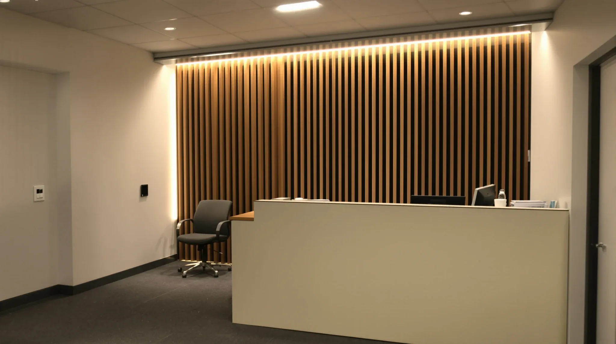 Office reception with the counter standing in front of a timber slat wall lit by a strip light along the top