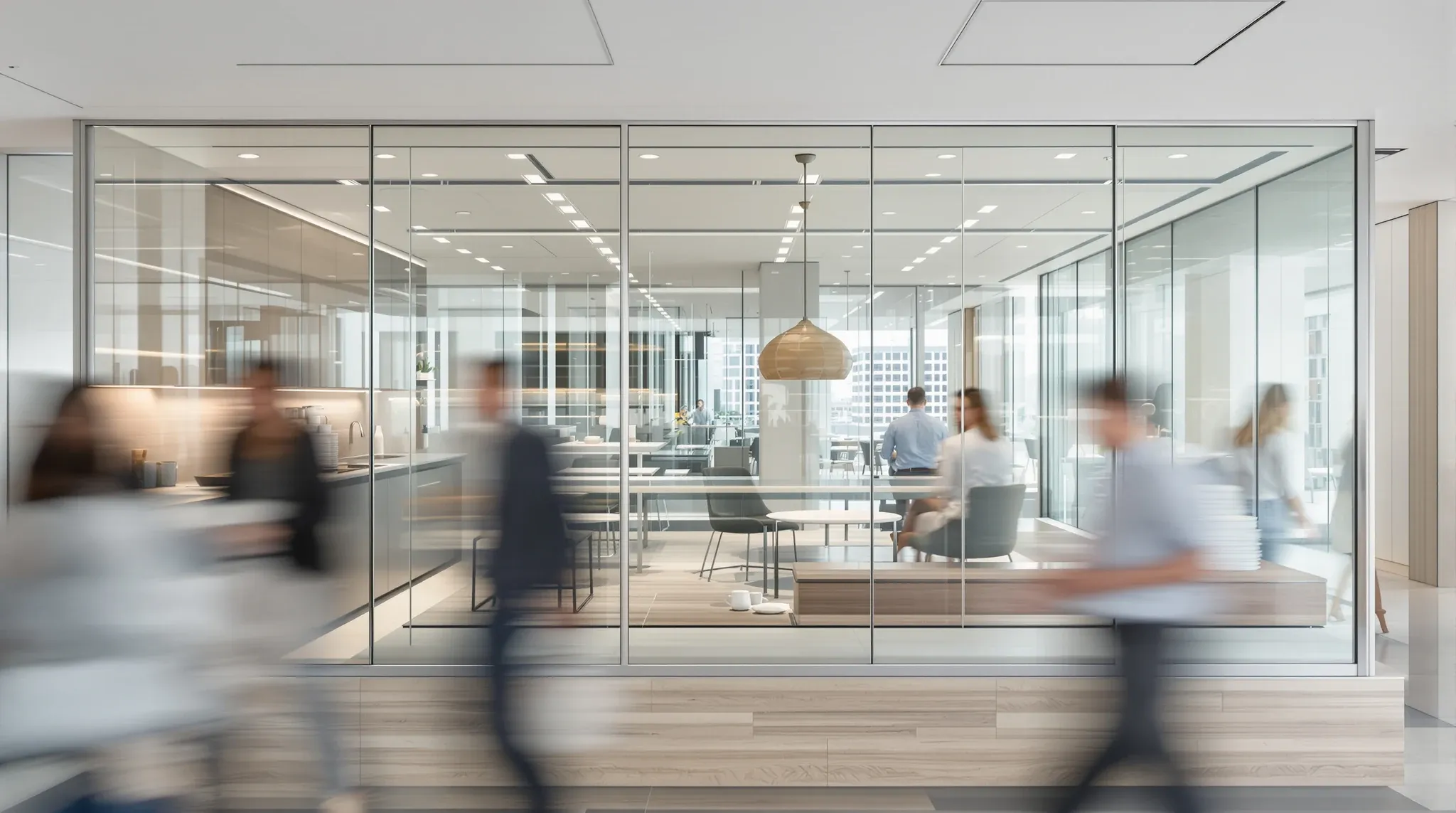 A glass meeting room right beside a busy office kitchen, with people blurred as they walk past