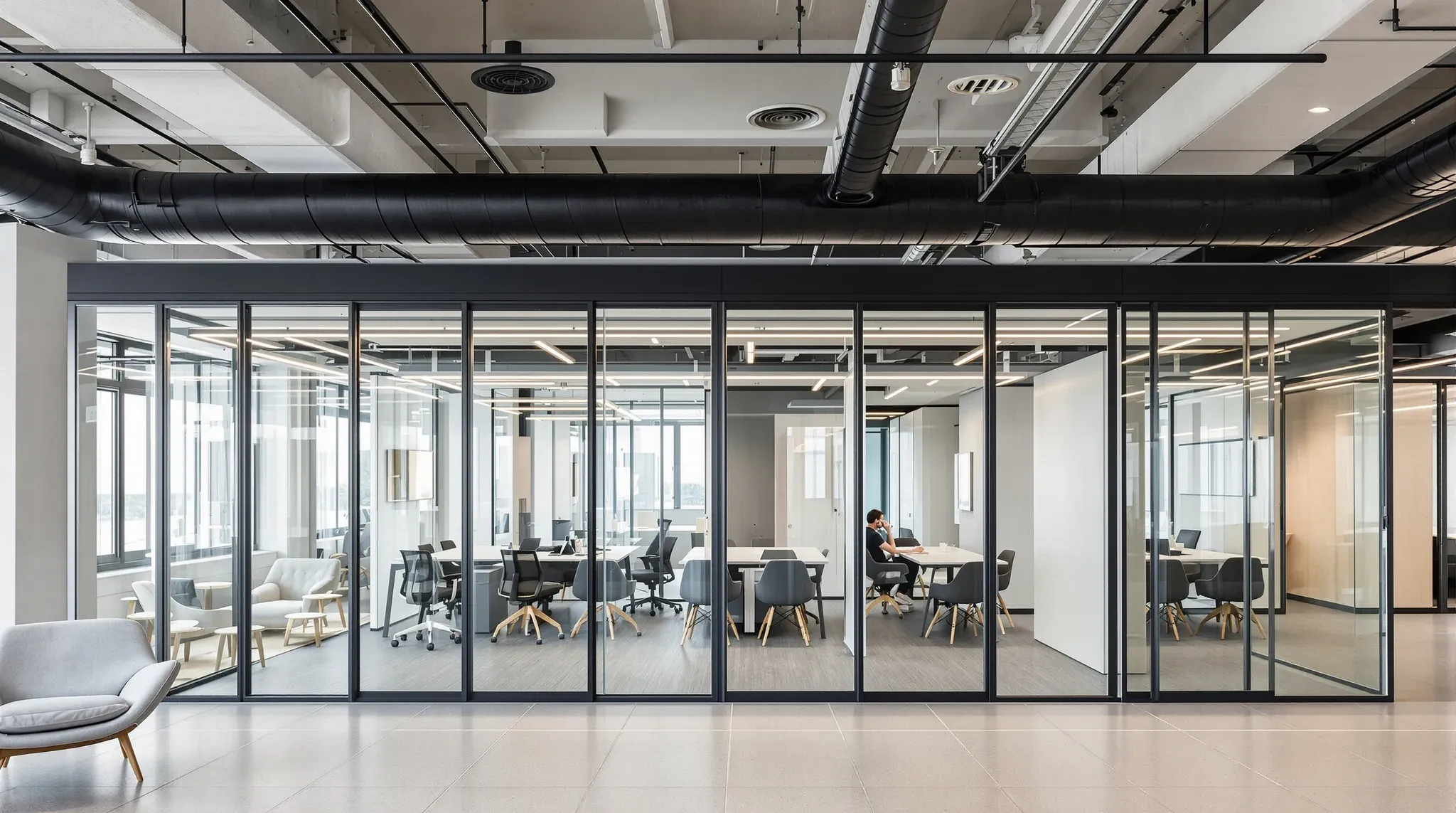 A demountable partition of glass and solid laminate modules in a coworking space with an exposed ceiling