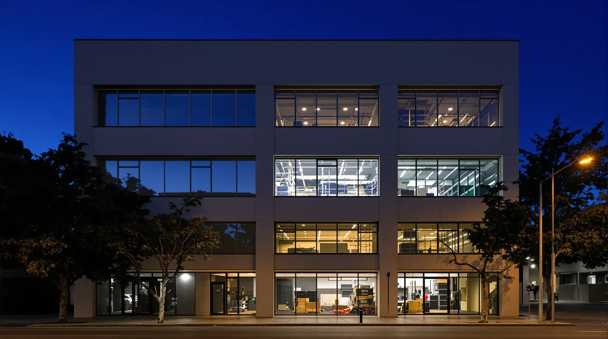 An office building at dusk with work lights glowing on one floor while the rest are dark
