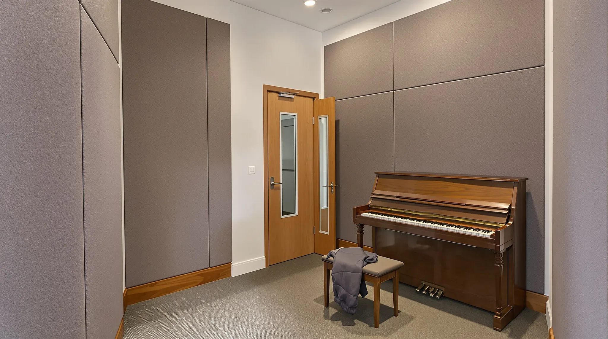 Music practice room with fabric acoustic wall panels, an upright piano and a door with a narrow vision panel