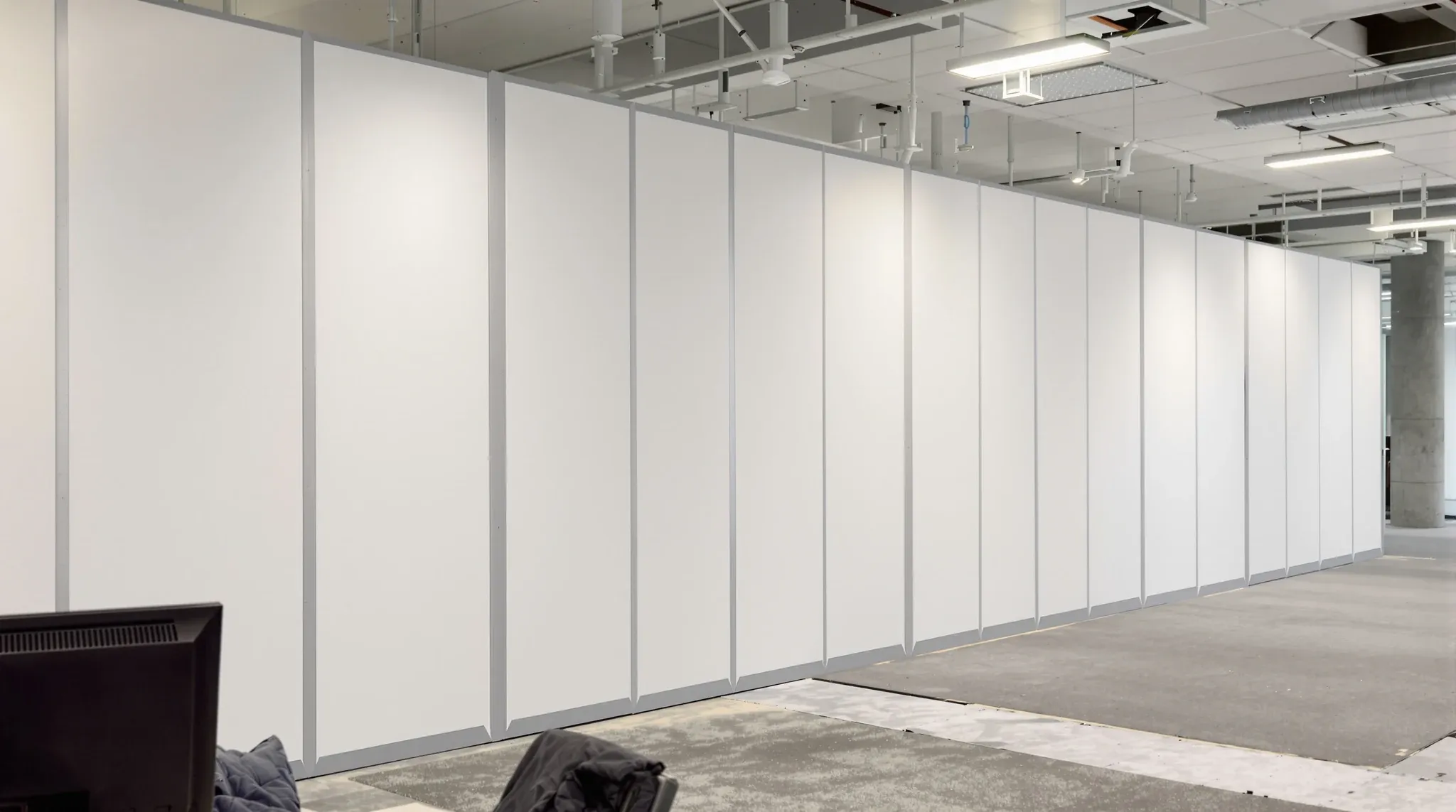A full-height white temporary hoarding closing off part of an office, with a working desk in front