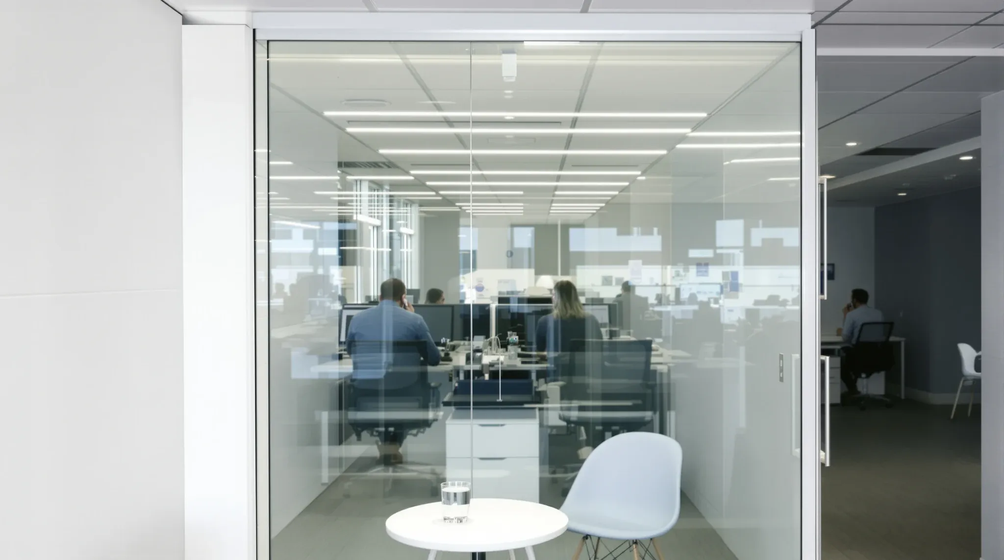 Busy workstations seen through the glass front of a small meeting room