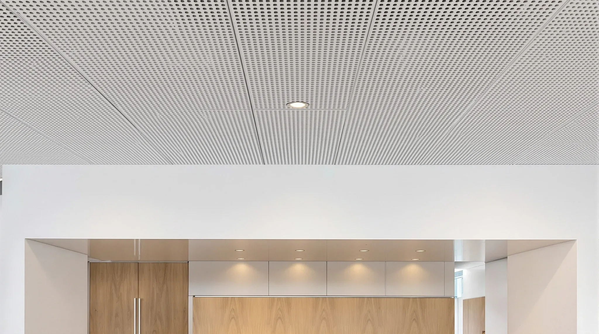 A perforated metal ceiling over an office reception beside a mineral fibre tile ceiling over the work area