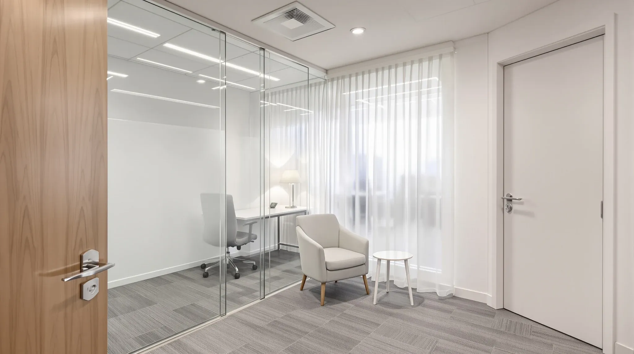 A consulting room with a desk and two chairs angled away from a glass wall screened by a sheer curtain