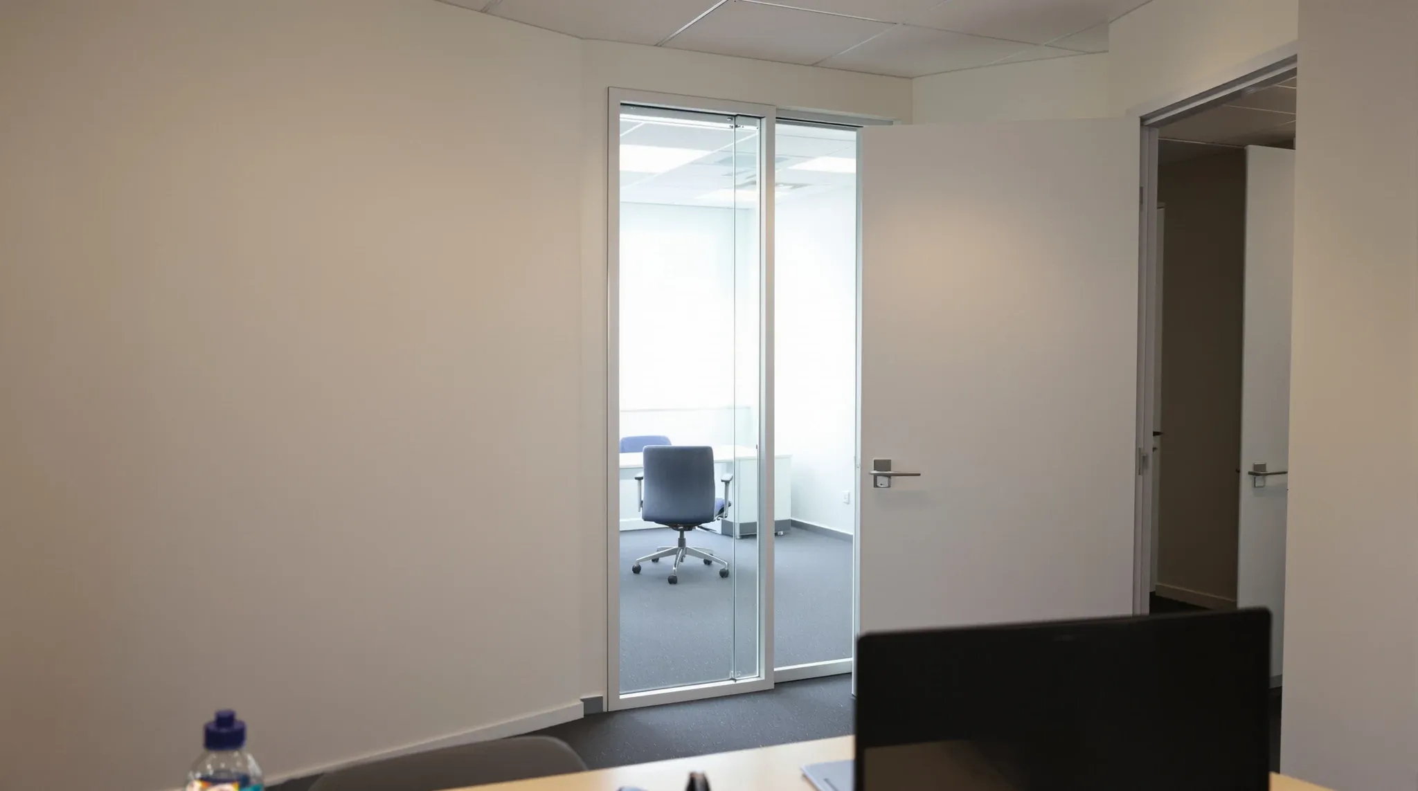 A painted plasterboard office wall with a narrow full-height glass panel beside a solid door