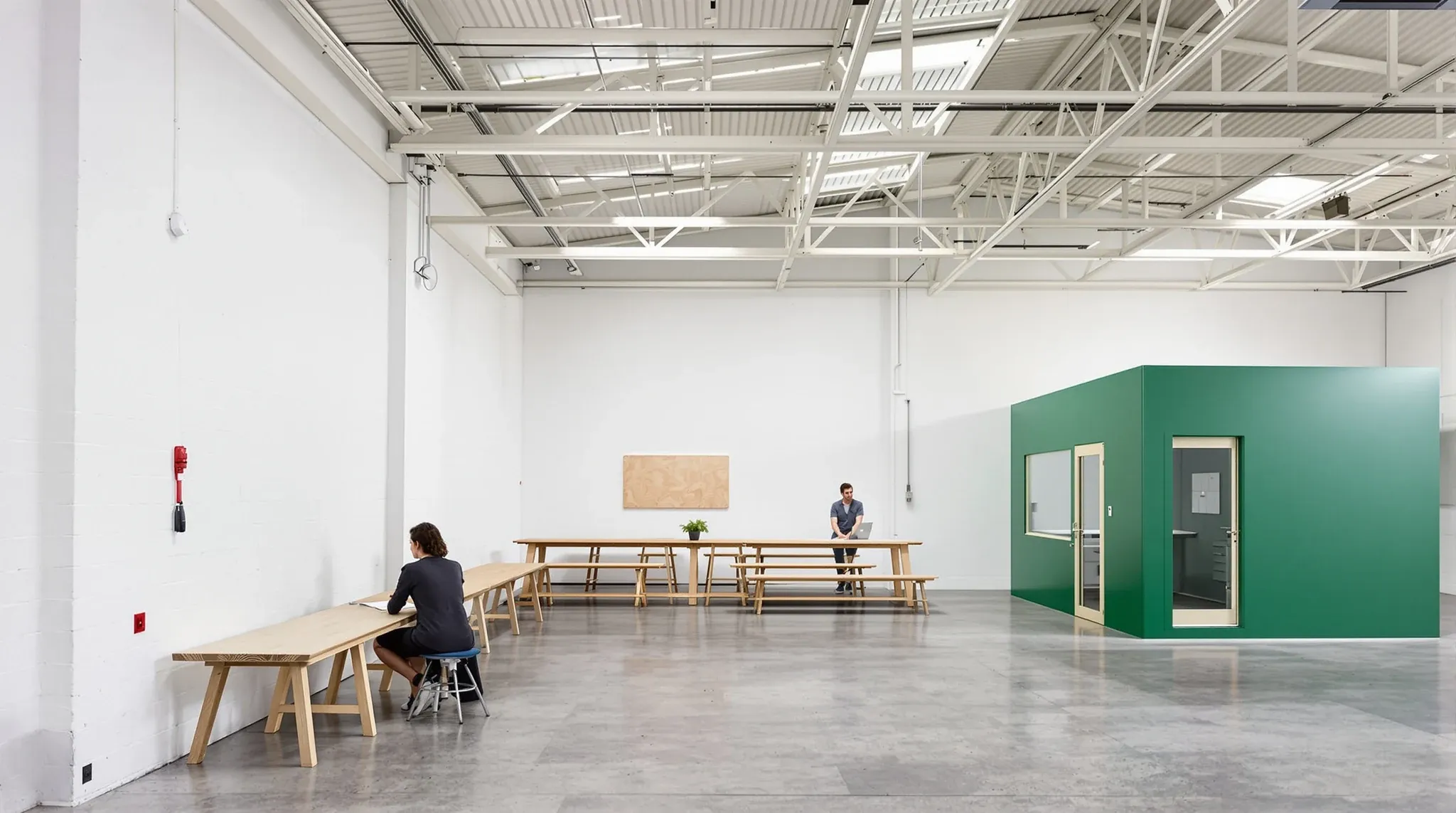 A modest studio fitout inside a light industrial unit with a green meeting room and a plywood desk bench