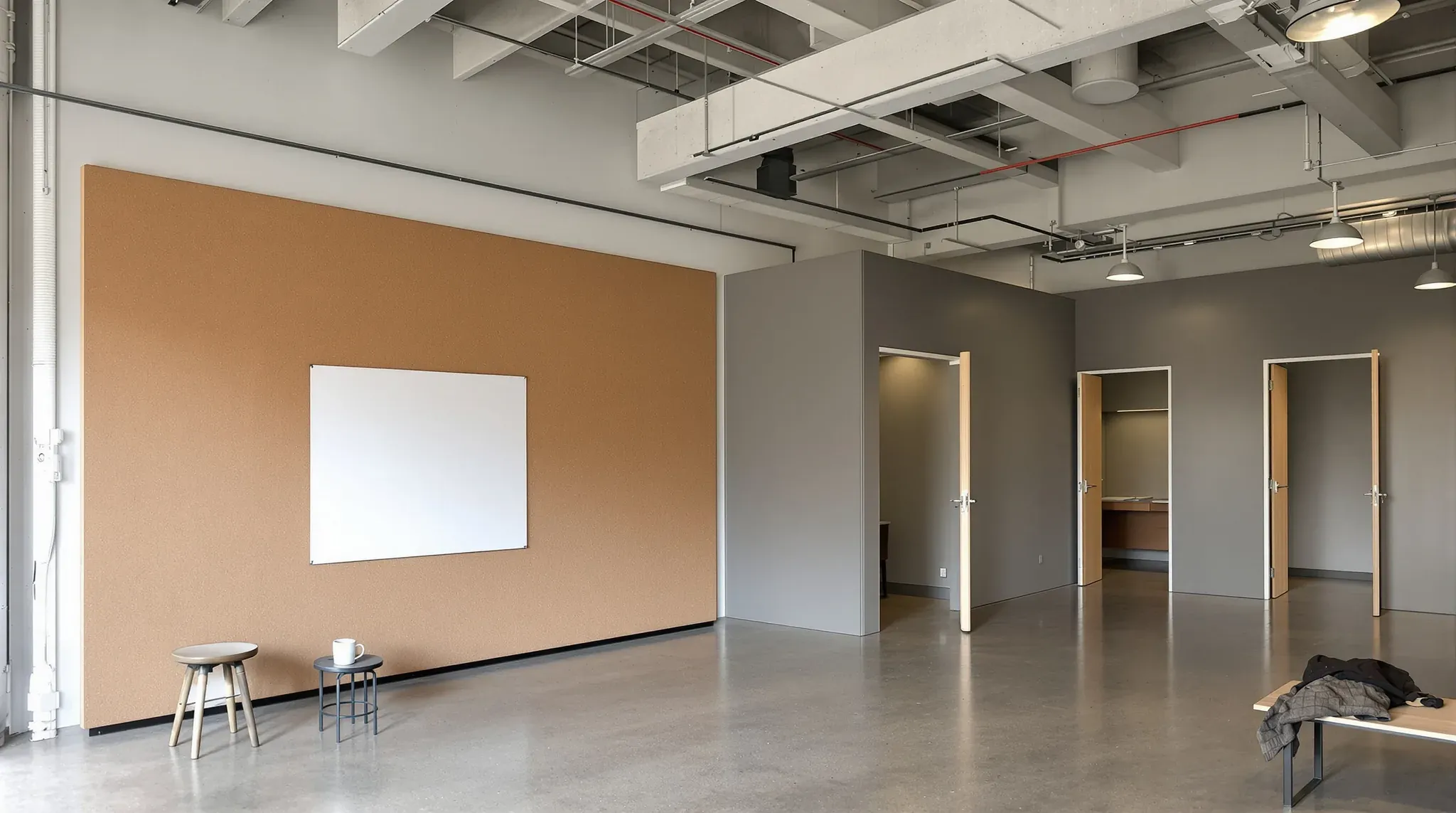 Agency floor with a cork pin-up wall, small grey edit suites with timber doors and an exposed ceiling