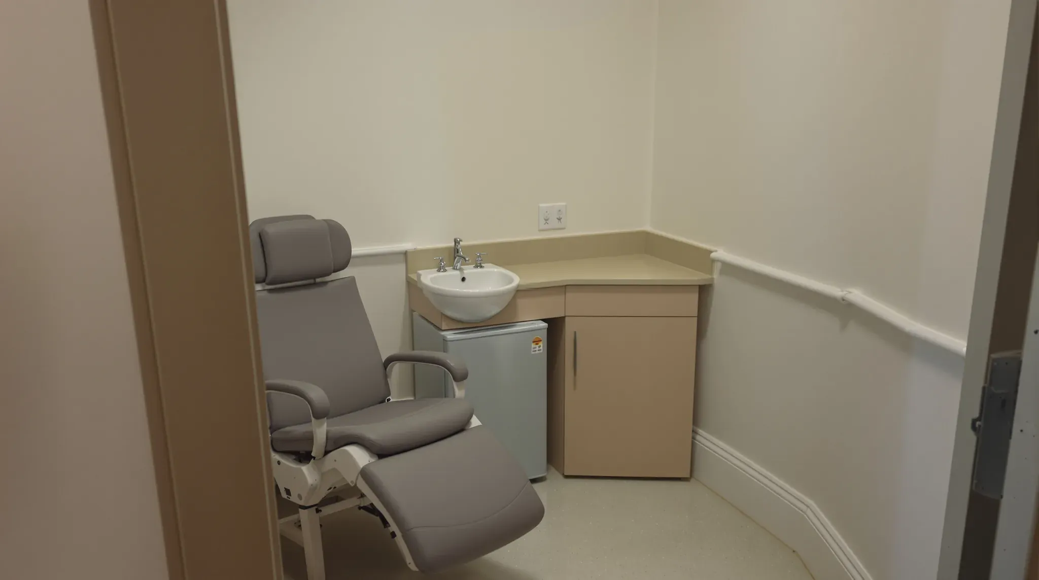 Small pathology collection room with a reclining chair, a hand basin on a vanity and an under-bench fridge